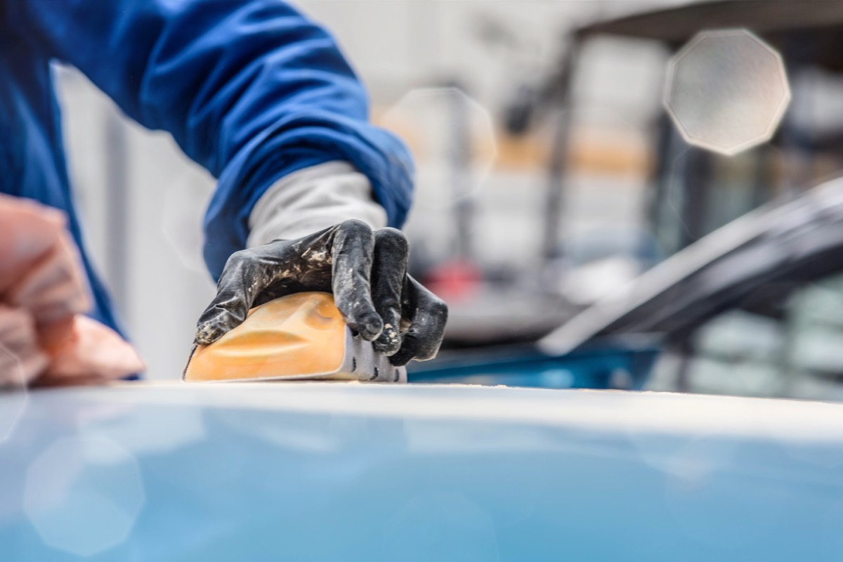 Mano con guanto nero che tratta la vernice del tetto di un'auto azzurra